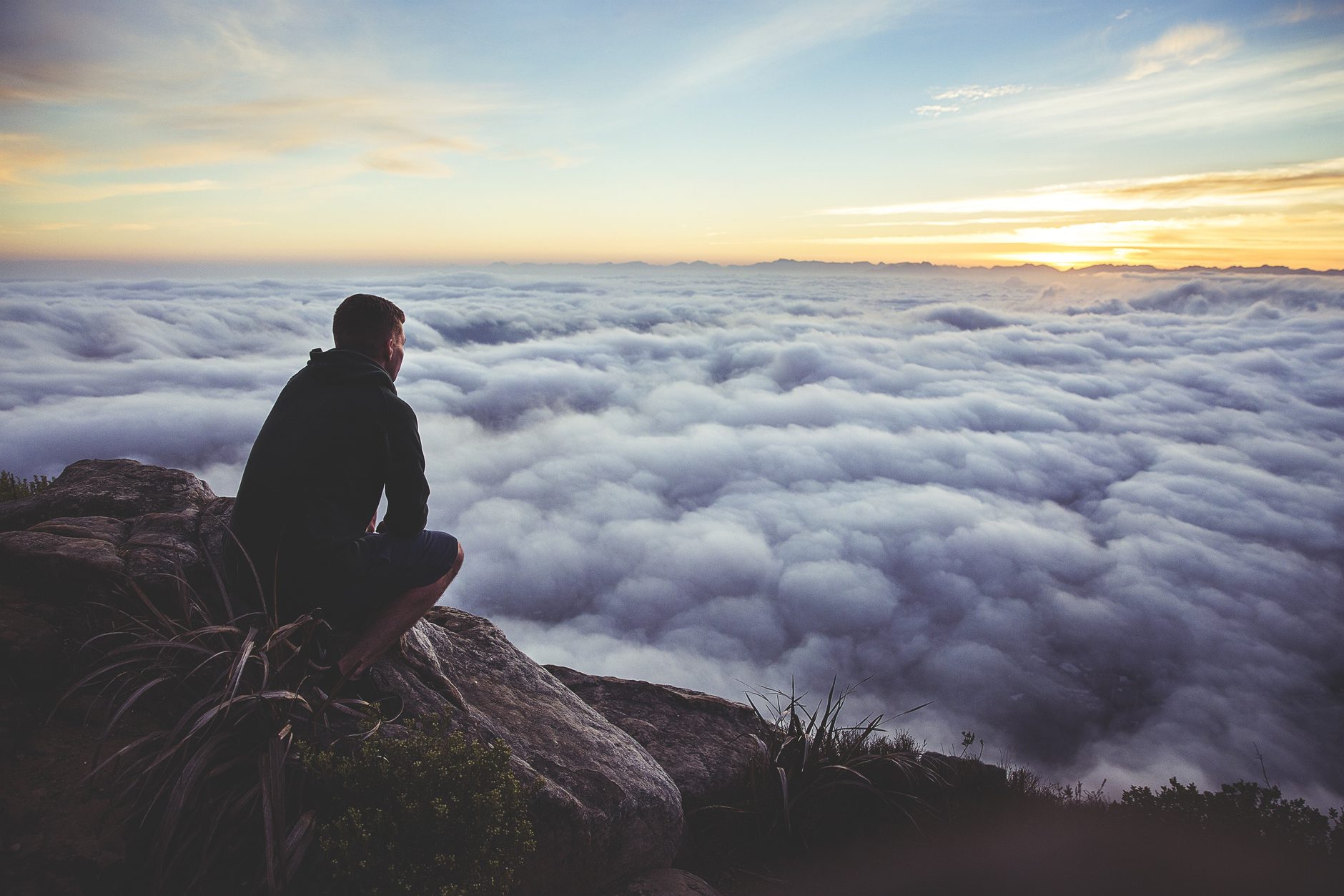 A person sitting on a rocky outcrop above a sea of cloud at sunrise